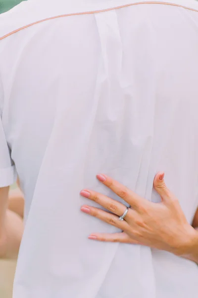 Close up hands of attractive young couple on a date walking together in park, hugging each other around the waist, back view