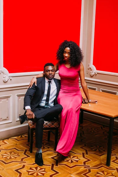 Portrait of handsome afro american businessman and beautiful african woman with red dress. Young couple hugging in the luxurious apartments