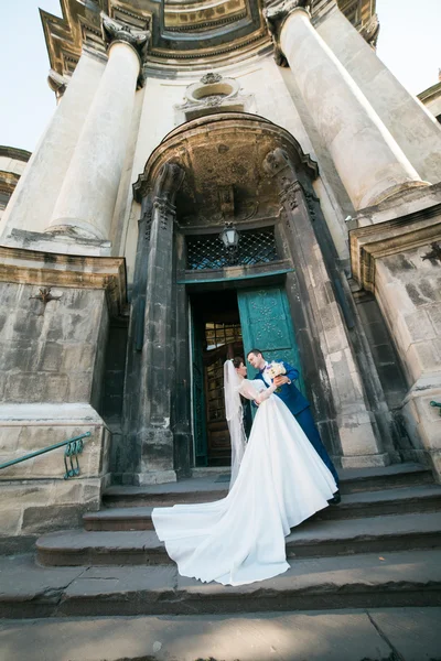 Romantic elegant newlywed couple posing near baroque column church