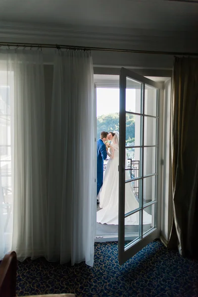 Beautiful young bride and groom kissing on the balcony in hotel room