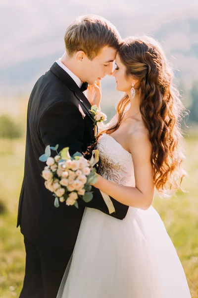 Newlywed young bride and groom with flower bouquet rubbing noses outdoors