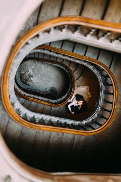 Handsome groom kissing beautiful brides neck on old wooden stairs indoors, top view
