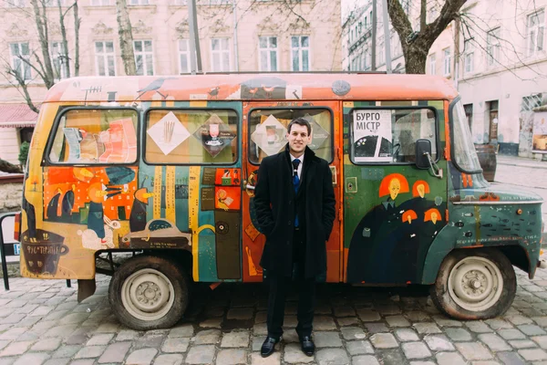 Smiling handsome man in black suit standing on colorful retro bus background