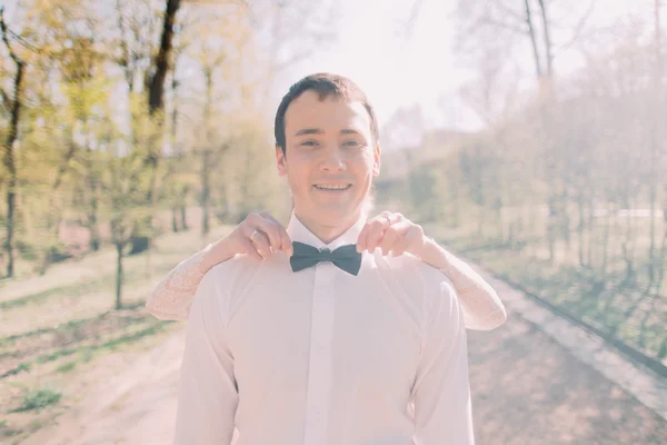 Bride standing behind fixing blue bow tie of her smiling groom in white shirt