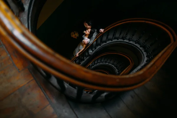 Handsome groom hugging from behind and kissing his beautiful sensual  bride holding bouquet at the wooden stairs