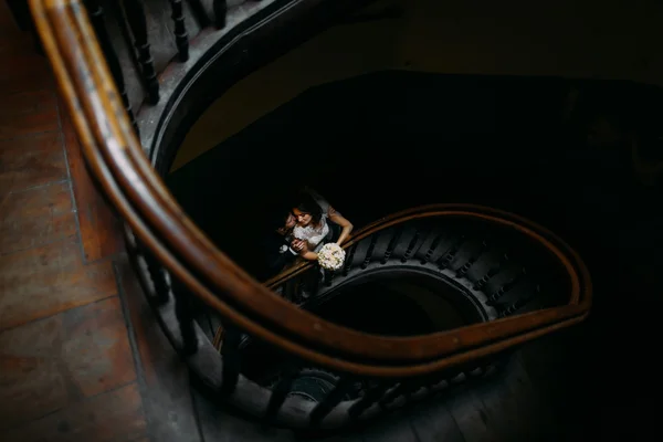 Handsome groom hugging from behind and kissing his beautiful sensual  bride holding bouquet at the wooden stairs