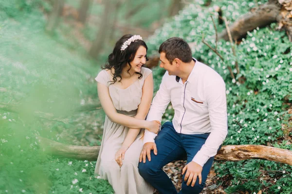 Beautiful woman and handsome man laughing on tree trunk in the meadow of spring flowers at sunny day