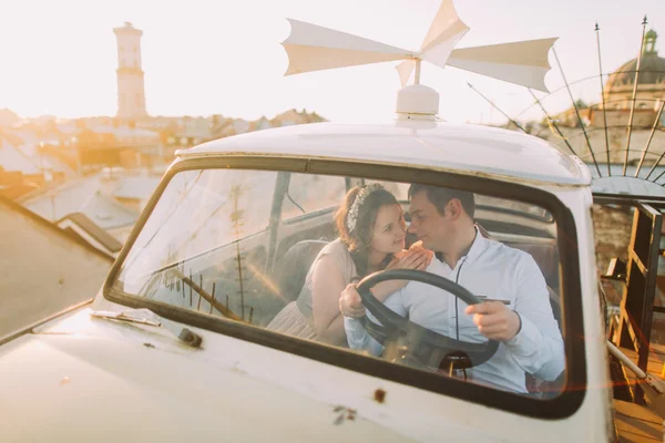 Young couple woman wearing floral headband and handsome man posing in white retro car on the roof