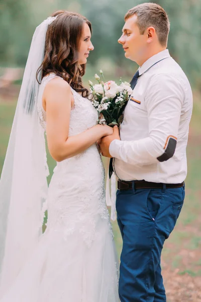 Bride and groom at wedding embracing face-to-face holding bridal bouquet in green park on spring nature