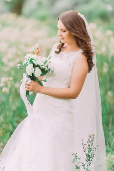 Beautiful elegant bride in wedding dress holding and looking at luxury natural white bridal bouquet