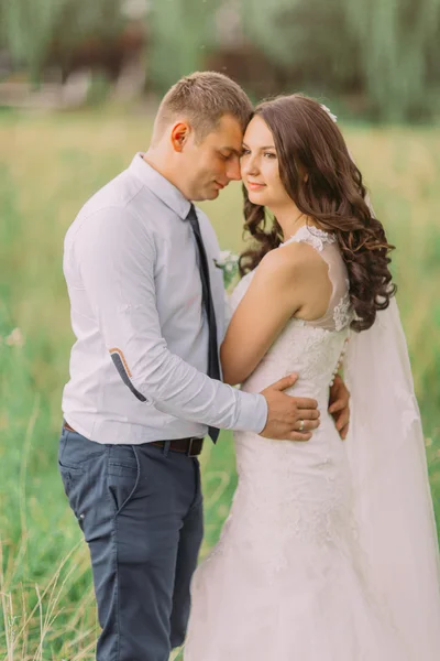 Man holds brides waist tenderly on the background of green forest