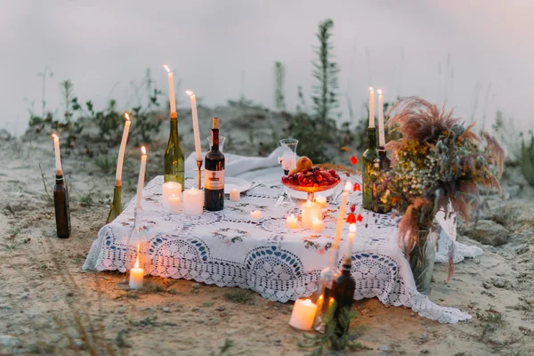 Outdoor table dinner setting with candles and wine on the beach at sunset