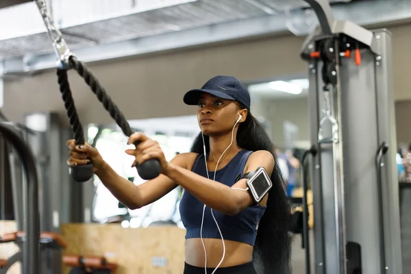 Sexy gorgeous african-american woman working out at the gym and listens to music in white earphones