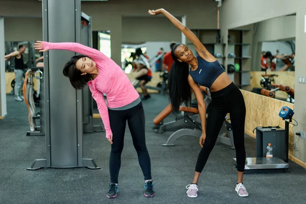 Slim black african-american fitness instructor and asian lovely woman doing exercise work together in the gym