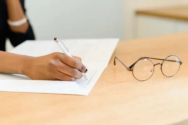 Close up of female hands writing in notepad on wooden desk with eyeglasses