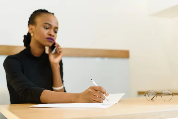 Serious confident young African or black American business woman on phone taking notes in office