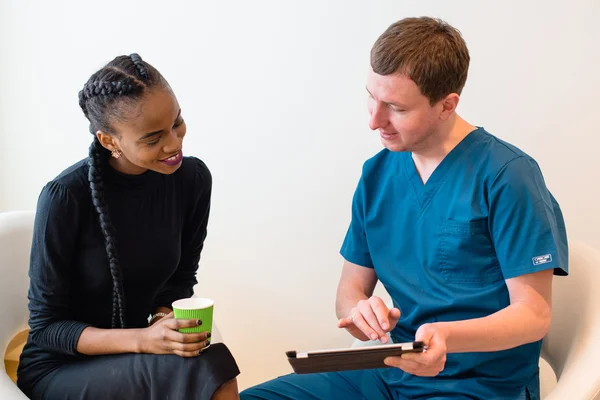 Portrait of confident, professional doctor wearing blue medical clothes with tablet and his smiling african or black american female patient