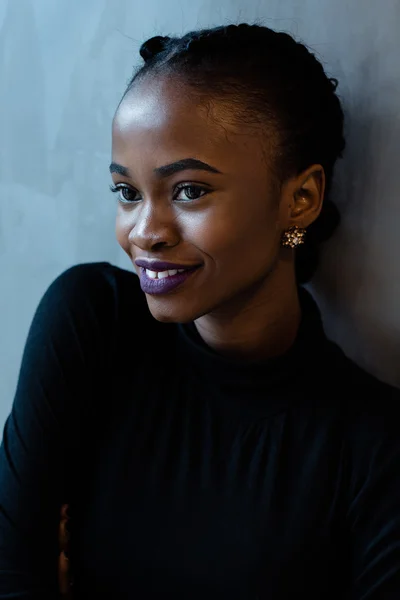 Portrait of smiling young african woman with bright violet lips looking away at gray background, close-up
