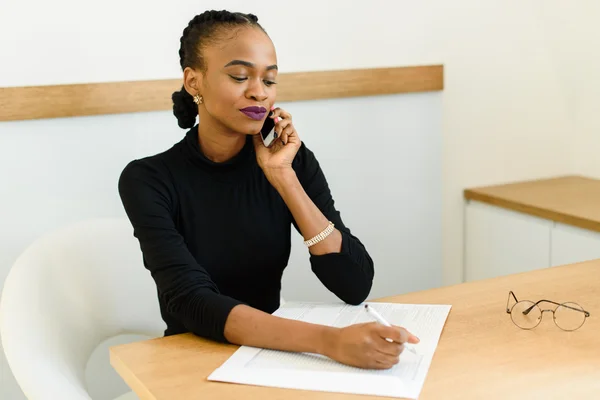 Serious confident young African or black American business woman on phone taking notes in office