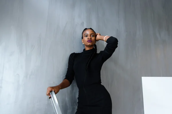 Young pretty black american woman touching her thick plait on dark studio background