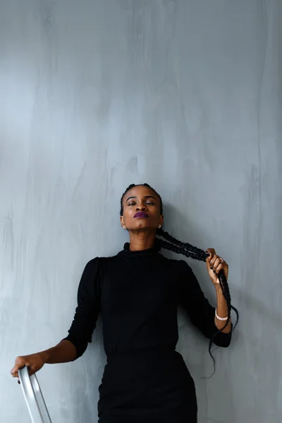 Young pretty black american woman touching her thick plait on dark studio background