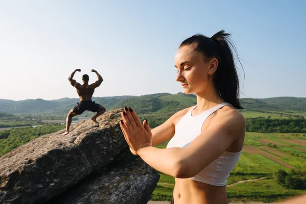 Mixed race couple sexy athlethic caucasian woman and african american bodybuilder practising yoga together. Training outdoor. Green rocky landscape background