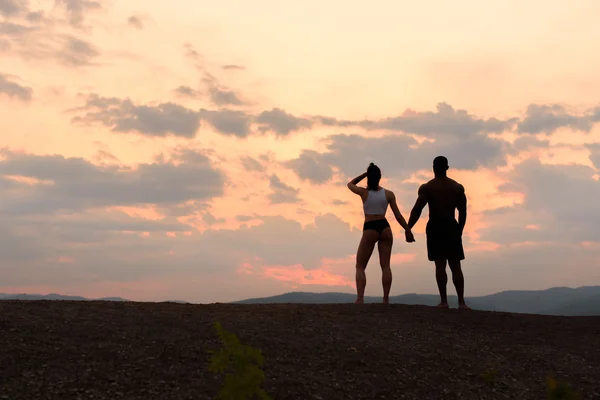 Silhouettes of athletic gymnastic couple watching the sunrise together. Beauty and perfection of humans body