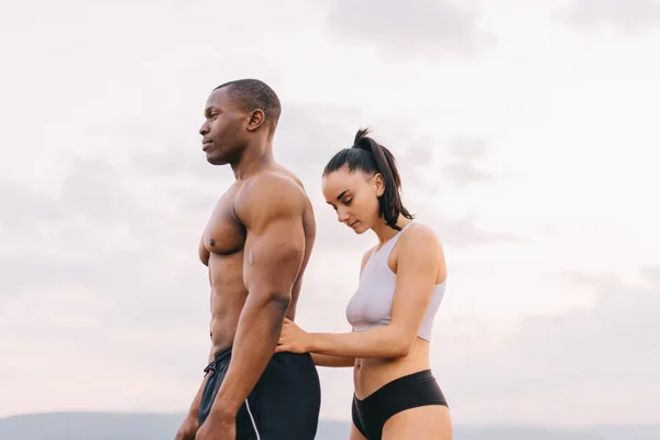 Portrait of beautiful muscular mixed race couple with perfect bodies in sportswear softly embracing on mountains landscape background.