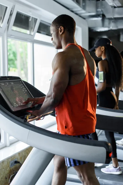 Muscular handsome black bodybuilder jogging on a treadmill in the gym
