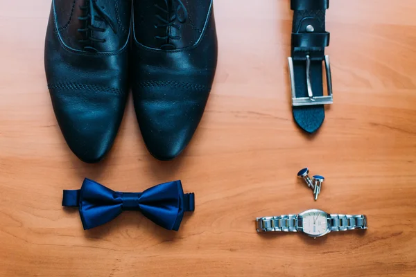 Close up of modern man accessories. Dark blue bowtie, leather shoes, belt, watch and cufflinks isolated on wood rustic background