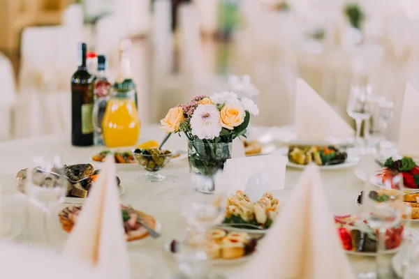 Finely served banquet restaurant table with snacks, cutlery, wine, glasses and flower decoration. European food