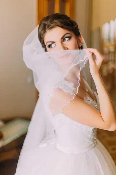 Beautiful bride in white wedding dress hiding her face behind the veil. Female portrait in bridal gown for marriage