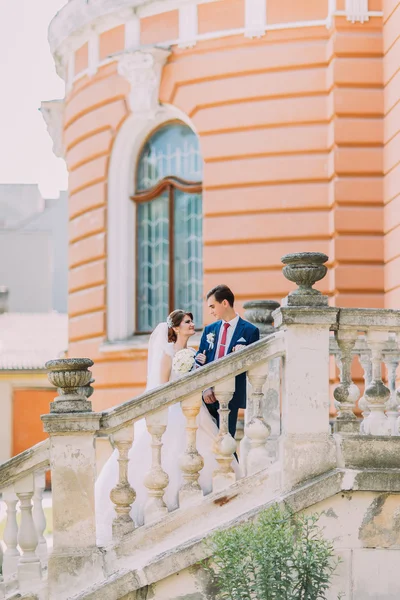 Beautiful young newlyweds on stairs in park. Old vintage building at background