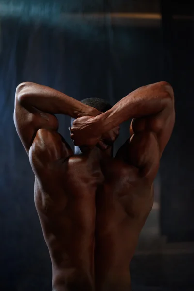 Back view of african american male body builder posing on a black studio background. Beauty and perfection of human body