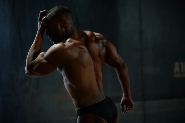 Sexy handsome african american male body builder posing on a black studio background. Beauty and perfection of human body