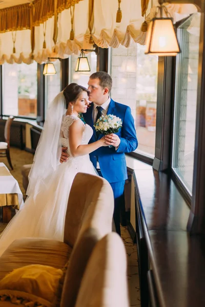 Sensual wedding couple. Beautiful bride and groom holding each other indoor near window