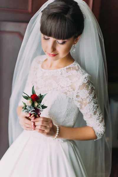 Beautiful bride posing with cute floral boutonniere indoors before her wedding