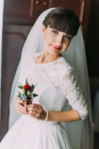 Beautiful bride with stylish hairlock posing when holding cute floral boutonniere in dressing room