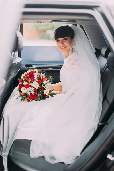 Charming young bride with her bridal bouquet in wedding car limousine