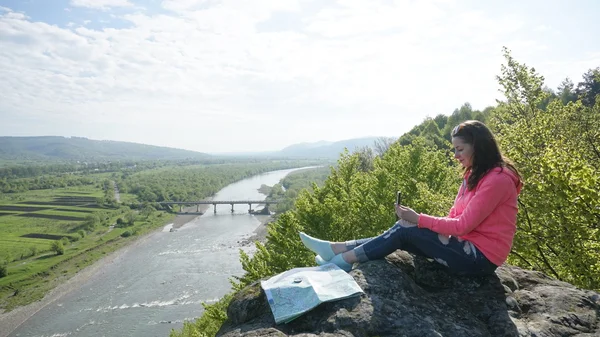 Happy young tourist woman sitting on the rocks with compass and map. Nature landscape background