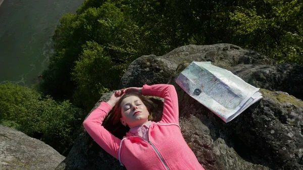 Harmony between human and nature. Young tourist woman lying on the rocks with compass, map