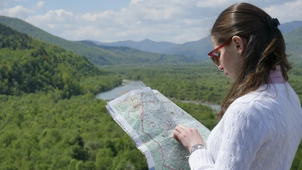Brunette tourist girl standing on the edge of green mountain and looking at map. Travel concept