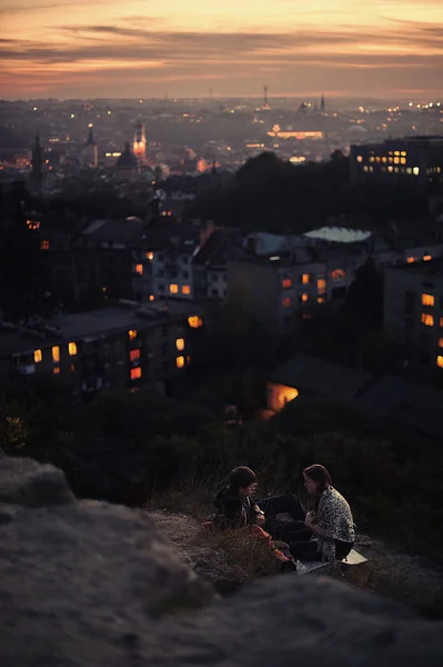 Young couple enjoying a beautiful sunset at their secret spot in Lviv, Ukraine. Bright city lights on background