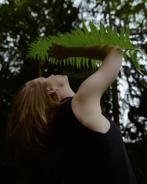 Calm young woman in shade of fern leaf, close-up view from below