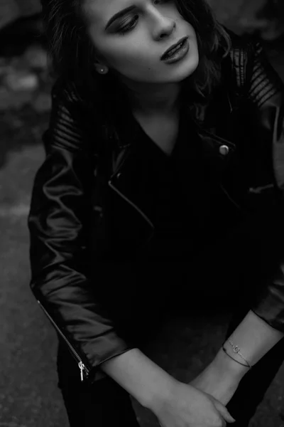 Blck and white close-up photo of young woman with bright makeup looking away sitting in black leather jacket