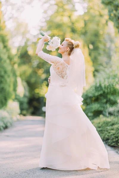 Beautiful emotional blonde bride with bouquet of white roses posing in the spring park