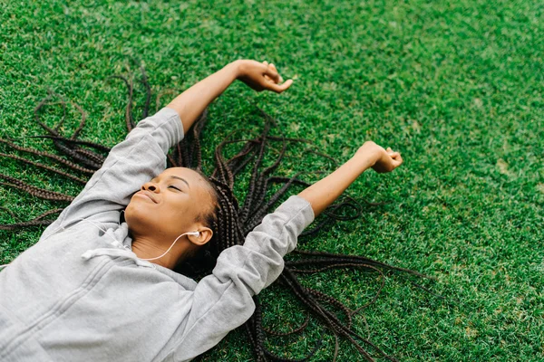 Outdoor portrait of a beautiful African American woman lying stretching hands on the grass with her braided hair and eyes closed