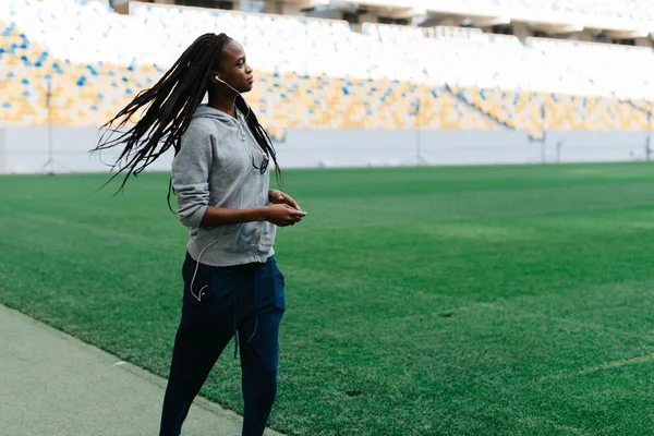 Attractive young African American woman in gray sportswear jogging at stadium