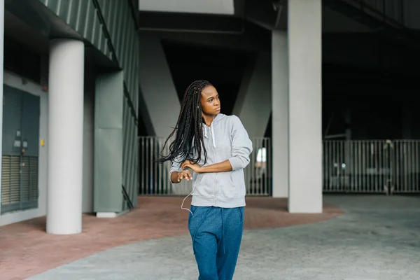 Half length portrait of young african american woman posing looking away against futuristic background, listening music with headphones