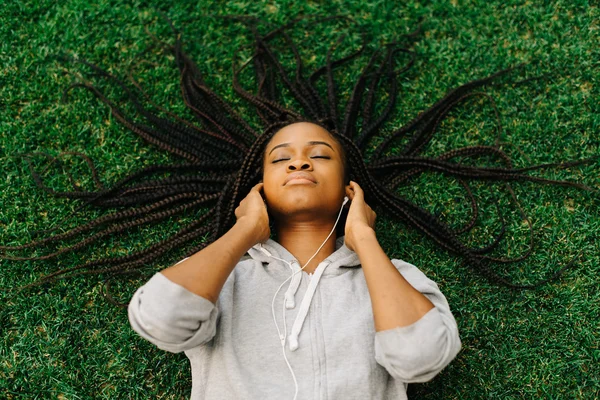 Portrait from above of a young african woman lying on grass with eyes closed and headphones